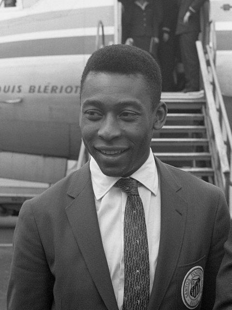 Pelé de terno e gravata, sorrindo em uma escada de avião.